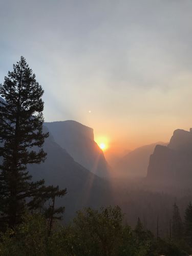 Sun setting through haze over a dark mountain valley