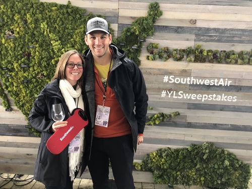 Allie and Chase holding wine glasses in front of a green wall
