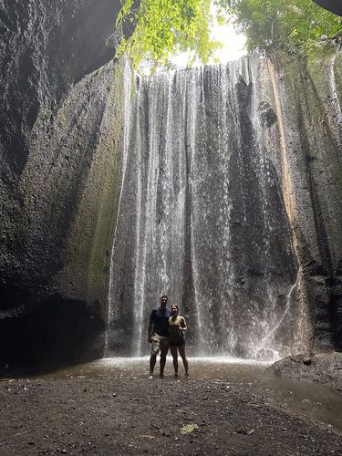 Two small figures standing in front of a tall waterfall