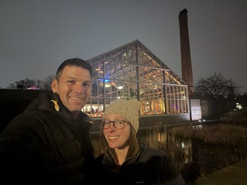 A couple at night by a glass-roofed building beside a canal