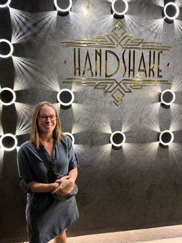 Allie standing under a lit “Handshake” sign