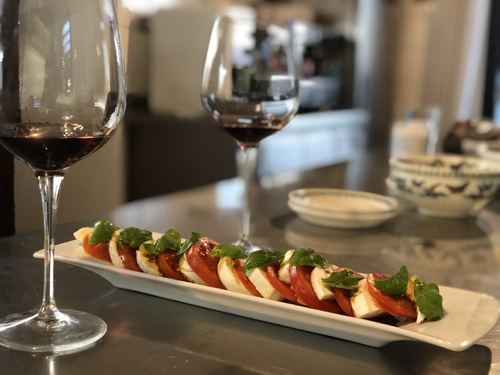 A glass of red wine beside a plate of tomato and mozzarella