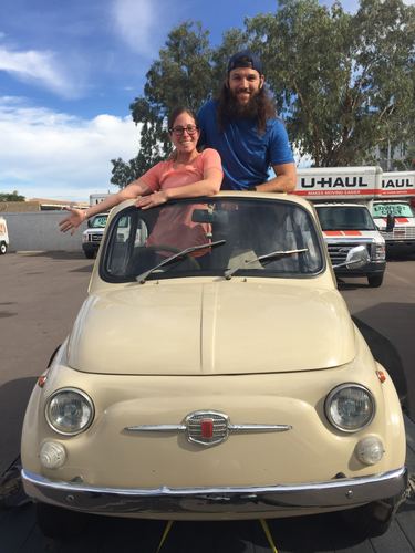 Allie and Chase leaning out of a cream-colored vintage Fiat 500