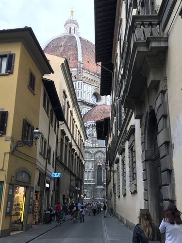 A narrow street with a cathedral dome at the far end