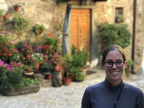 Allie standing by a wooden door surrounded by flowers