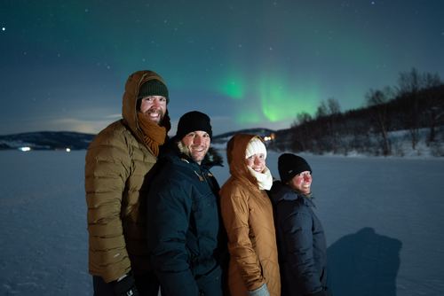 Four people in winter coats under the northern lights