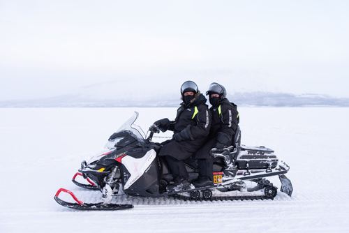 Two people riding a snowmobile across a frozen white landscape